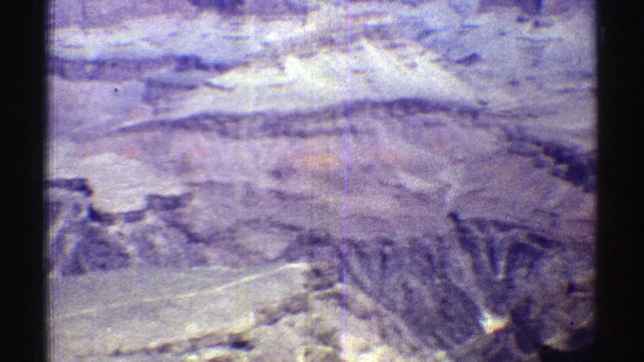 High view across a canyon rim with pale desert rock, dark slopes, and film gate edges.