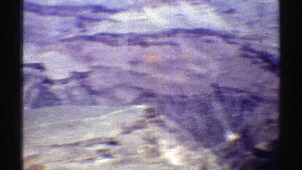 Soft 8mm aerial frame of Arizona mesa and canyon terrain, with red-grey rock bands and visible film wear.