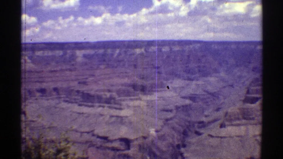 1969 Arizona 8mm frame showing a wide desert canyon with layered rock formations, distant horizon, and blue sky with clouds.