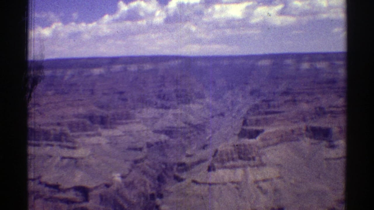 Canyon panorama with eroded rock shelves, distant horizon, clouds, and dark film borders.