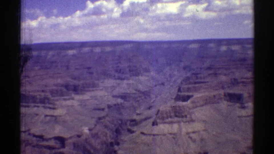1969 Arizona home-movie frame of a broad canyon panorama with eroded rock shelves and scattered clouds above the horizon.