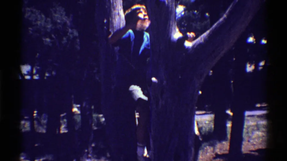 The child appears higher beside the trunk, wearing a dark blue shirt and light shorts in metadata-supported 1969 Arizona 8mm footage.