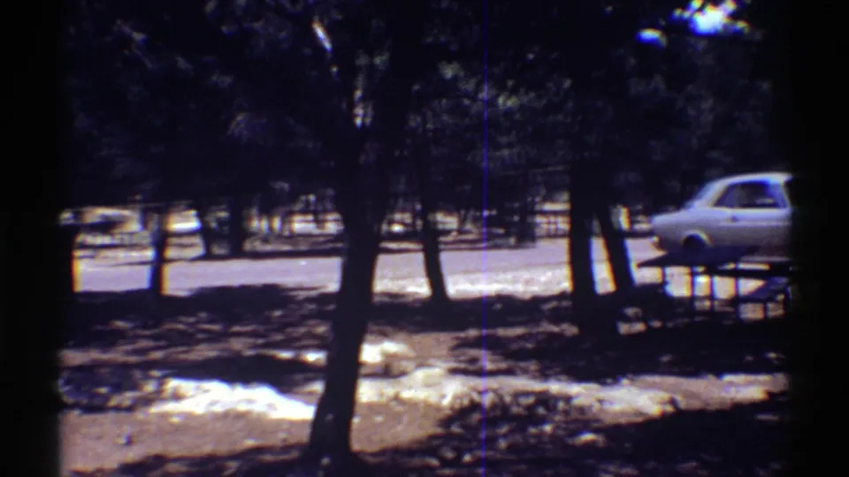 1969 Arizona travel footage frame with classic cars partly obscured by trees near a bright parking roadway.