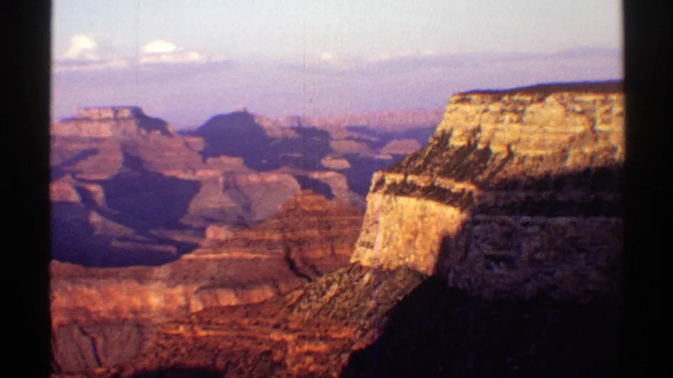 1969 8mm Arizona home-movie frame showing the Grand Canyon with sunlit cliff edges, shadowed slopes, distant formations, and faded color.