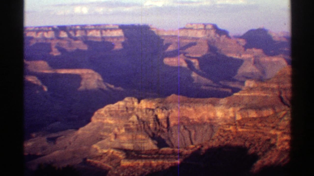 1969 8mm view of Arizona's Grand Canyon, with sunlit foreground rock, layered rims, and deep blue-purple canyon shadows.