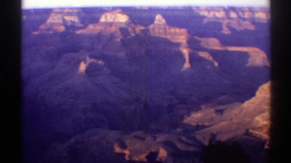 Arizona Grand Canyon view on aged 8mm film, with distant buttes, deep ravines, and visible vertical scratches across the frame.