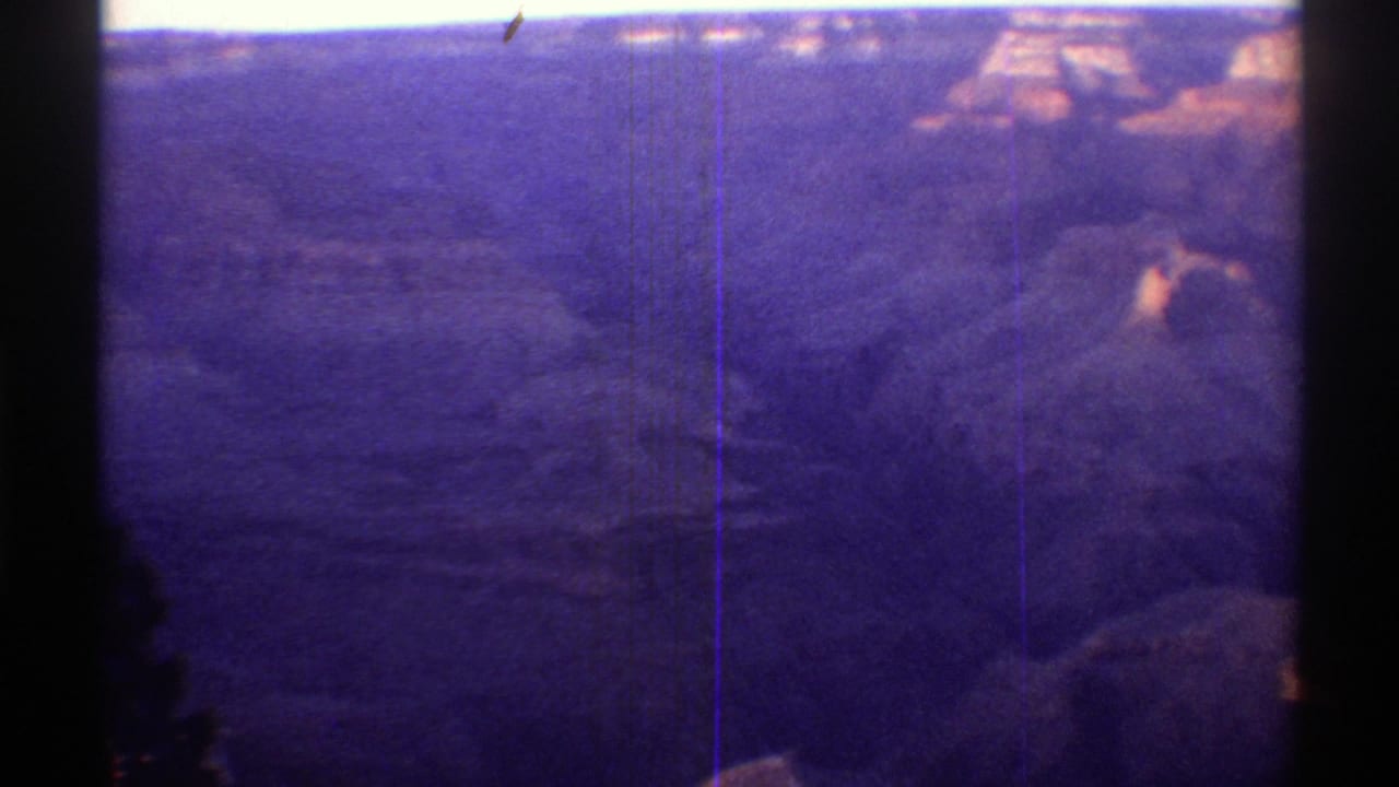 Canyon panorama with distant mesas, shadowed valley floor, and a dark vertical frame edge at left.