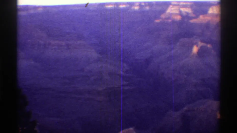Arizona canyon terrain from a 1969 8mm home movie, showing distant mesas, deep valley shadows, and purple-shifted film color.