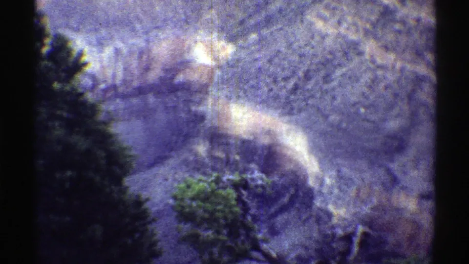 Arizona home-movie frame showing evergreen foreground trees against layered canyon terrain and soft haze.