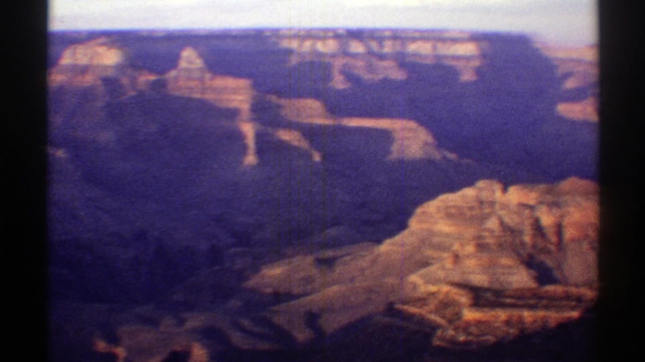 Wide canyon vista with layered cliffs, shadowed ravines, and hazy sky.