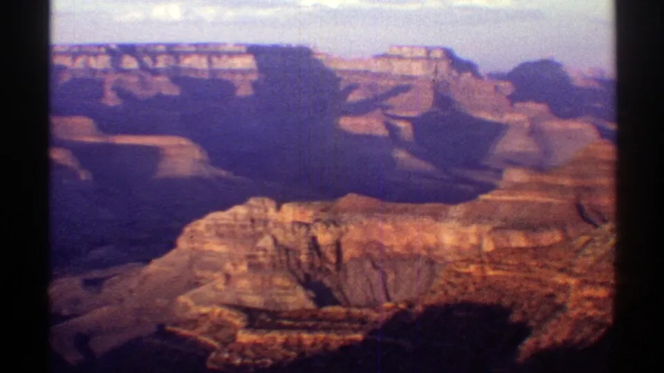 Vintage 8mm frame of the Grand Canyon in Arizona, with red rock ridges, distant mesas, and visible film grain and vertical lines.
