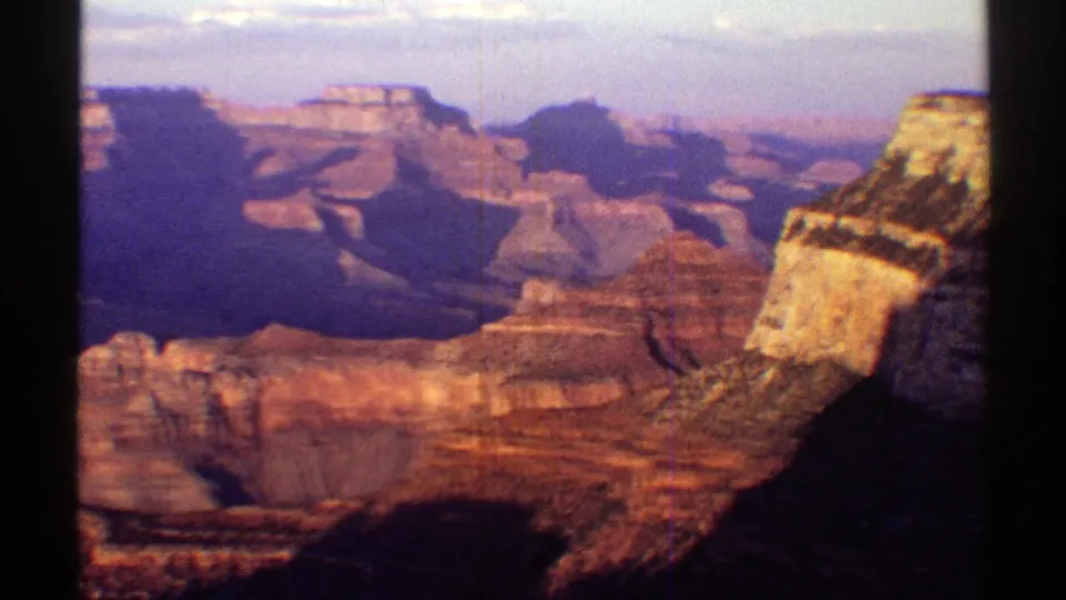 1969 Arizona home-movie frame looking over the Grand Canyon, with a foreground rim, distant rock walls, purple haze, and dark film edge.