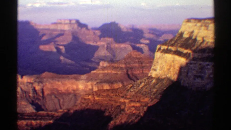 1969 Arizona 8mm frame showing layered red canyon walls, distant mesas, haze, and dark foreground framing.