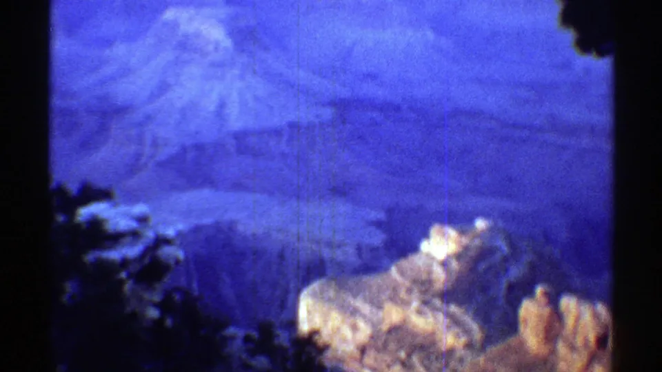 1969 Arizona 8mm frame showing a hazy canyon overlook with foreground trees and pale sunlit rock forms.