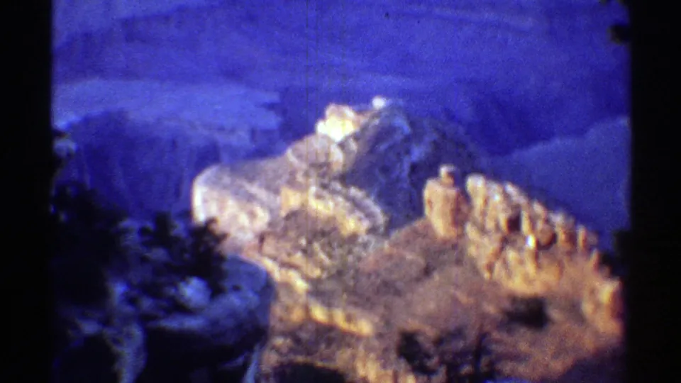 1969 Arizona 8mm frame showing a sunlit rocky ridge, dark foreground trees, and blue canyon walls beyond.