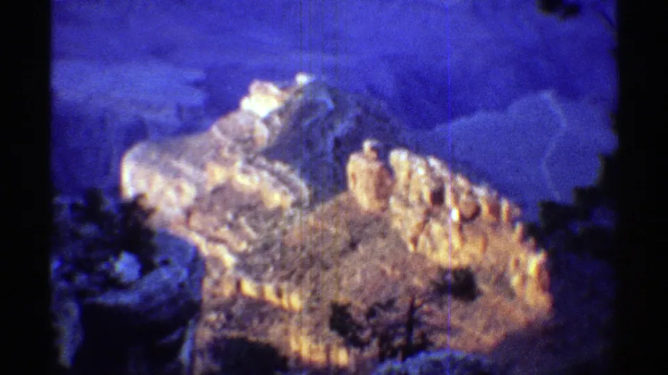 1969 Arizona 8mm frame showing an illuminated rugged rock formation surrounded by blue twilight shadow and soft film grain.