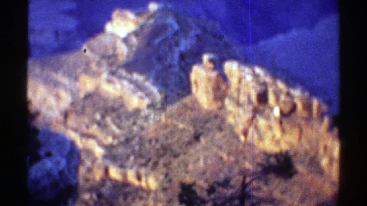 1969 Arizona home-movie frame with a zoomed view of warm orange rock layers set against shadowed blue desert terrain.