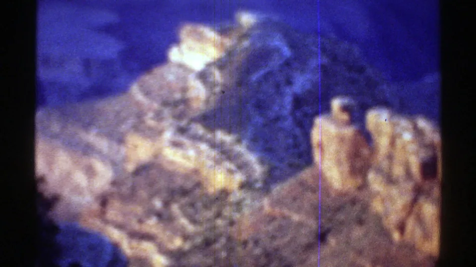 1969 Arizona home-movie frame with illuminated rock spires, dark ridges, blue shadows, and visible film wear.
