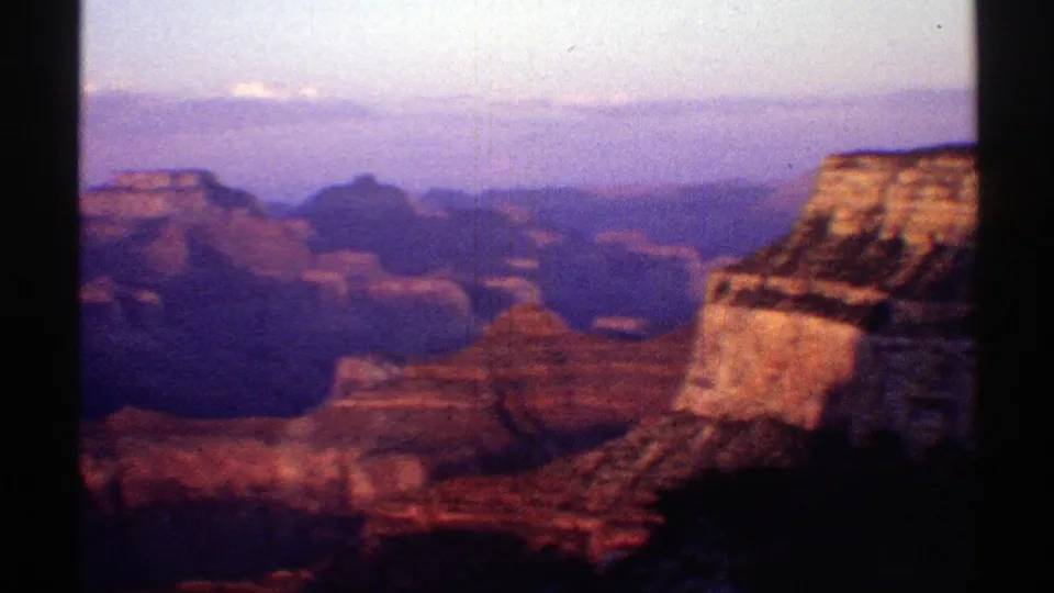 1969 Arizona 8mm panorama of the Grand Canyon, with layered cliffs, distant mesas, haze, and a sunlit outcrop at the right edge.