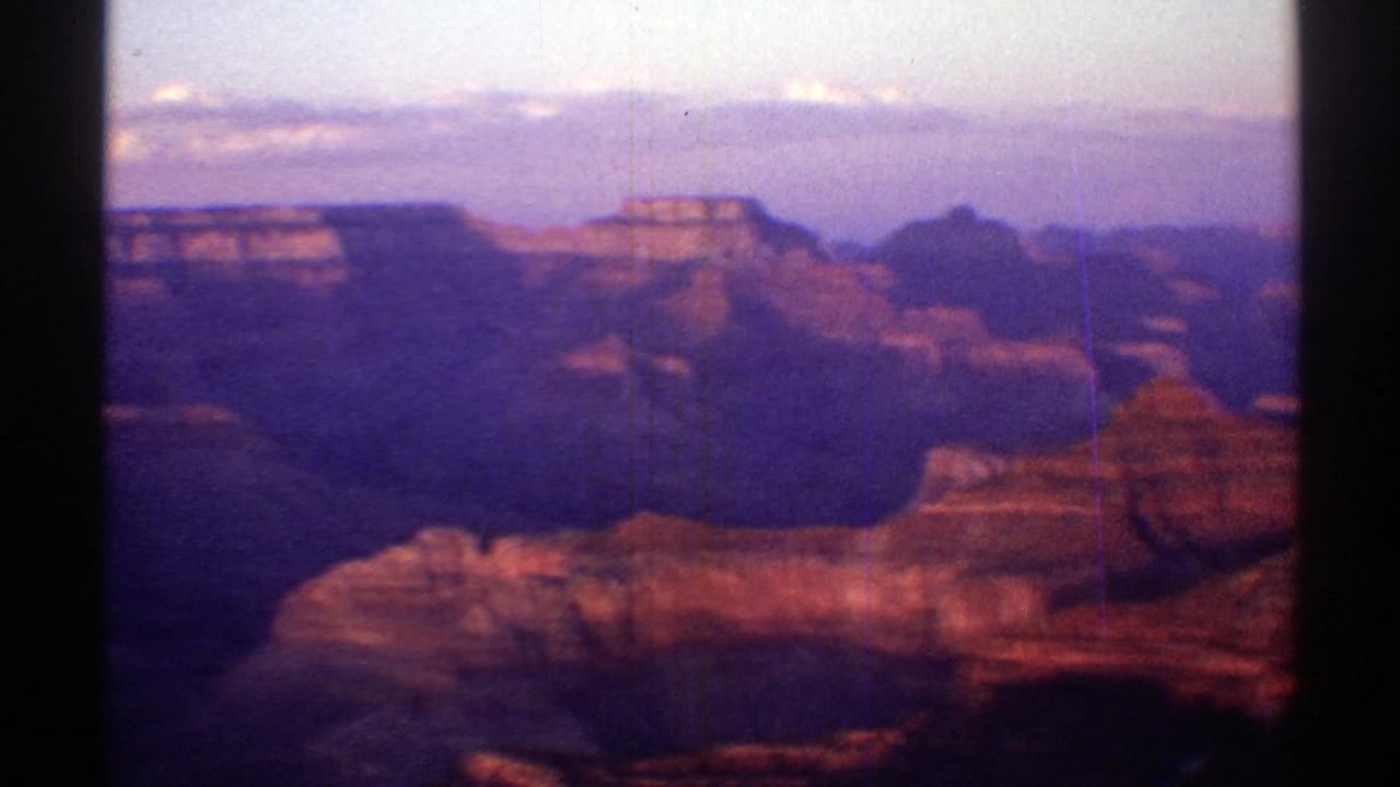 1969 Arizona home-movie frame showing layered canyon formations, shadowed ravines, and a soft twilight sky.