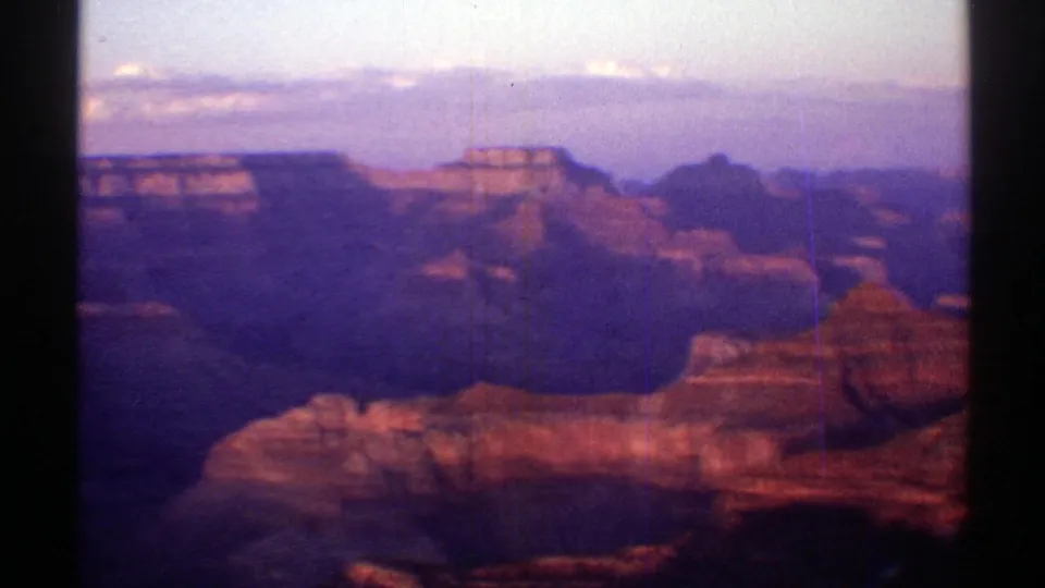 1969 Arizona home-movie frame showing layered canyon formations, shadowed ravines, and a soft twilight sky.