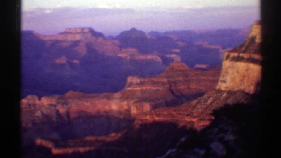 1969 Arizona 8mm frame of the Grand Canyon, showing layered red cliffs and a pale vertical rock face on the right side.