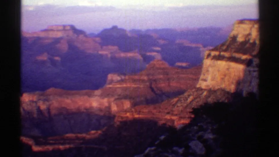 1969 Arizona home-movie frame showing the Grand Canyon at sunset, with warm rock ledges and distant blue-purple canyon shadows.
