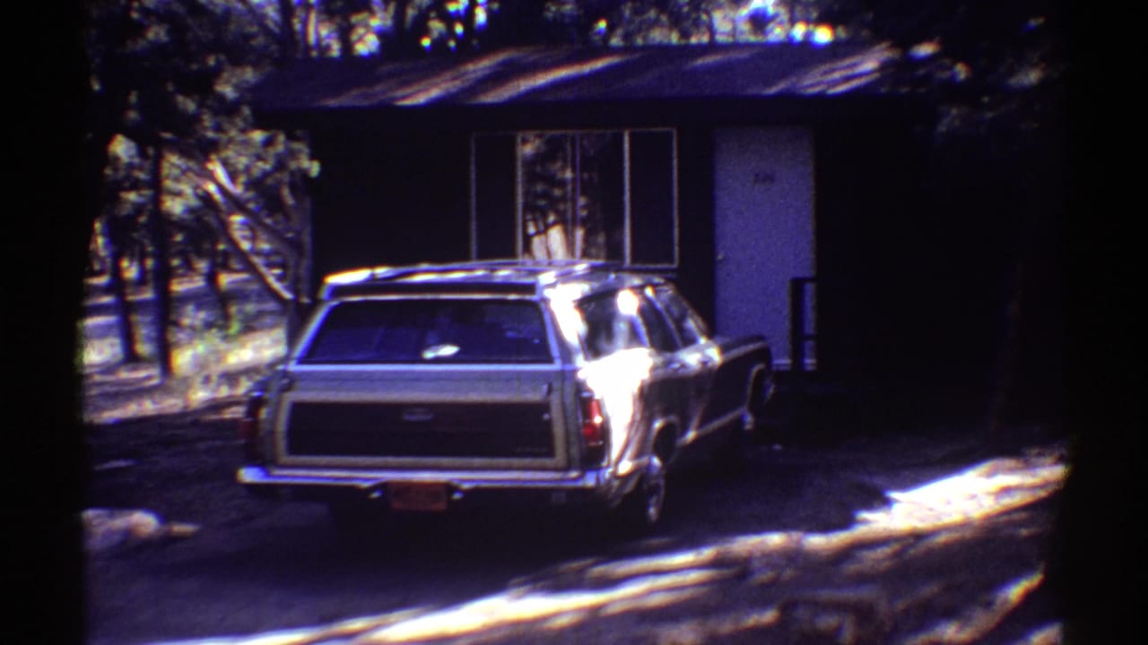 Light-colored station wagon parked at a wooded cabin stop in the Arizona 1969 home-movie sequence.