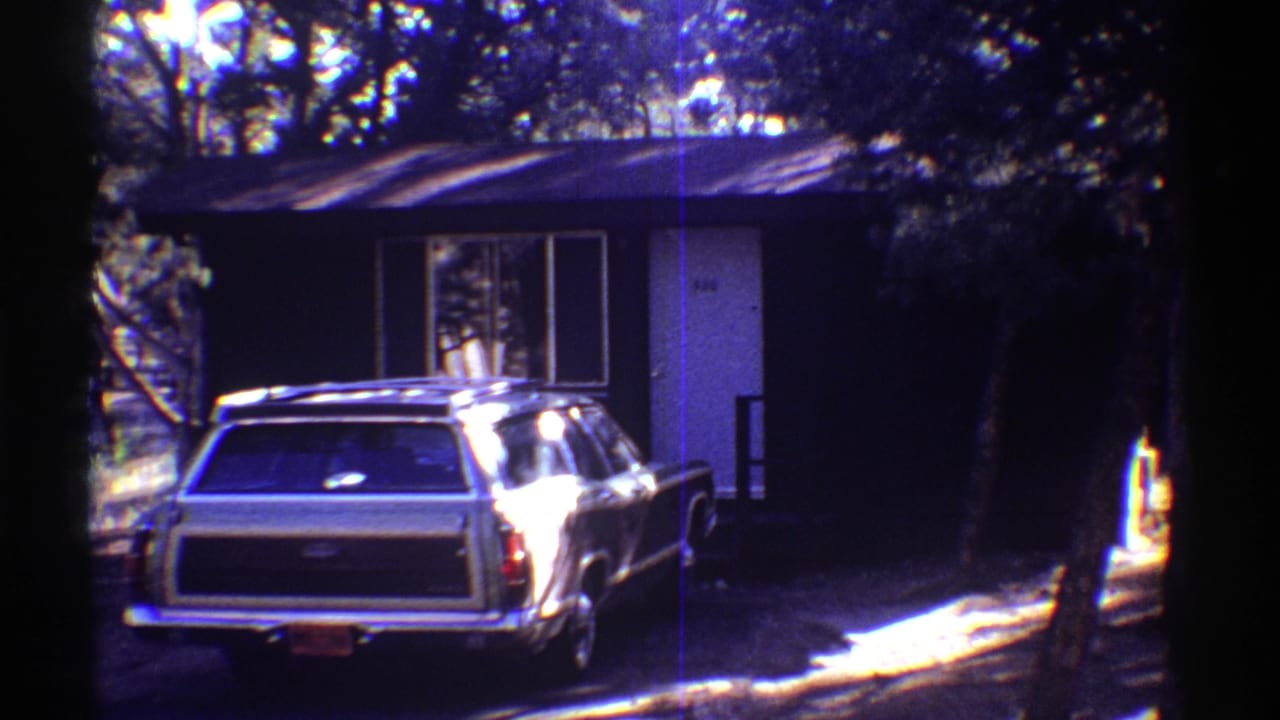 1969 Arizona 8mm frame showing a large station wagon parked near a small dark-sided house in deep tree shade.