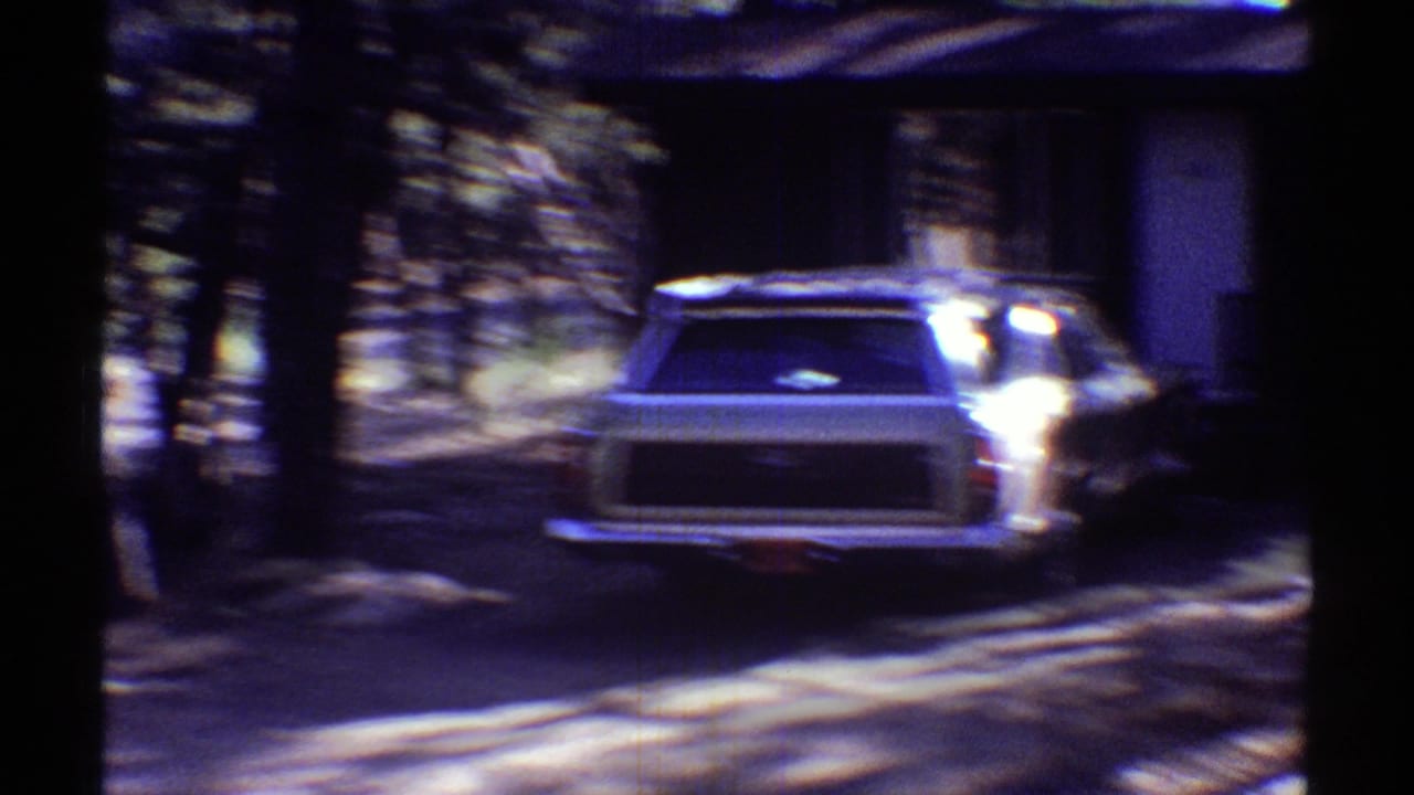 1969 Arizona 8mm frame showing a station wagon in a shaded residential driveway with trees and soft motion blur.