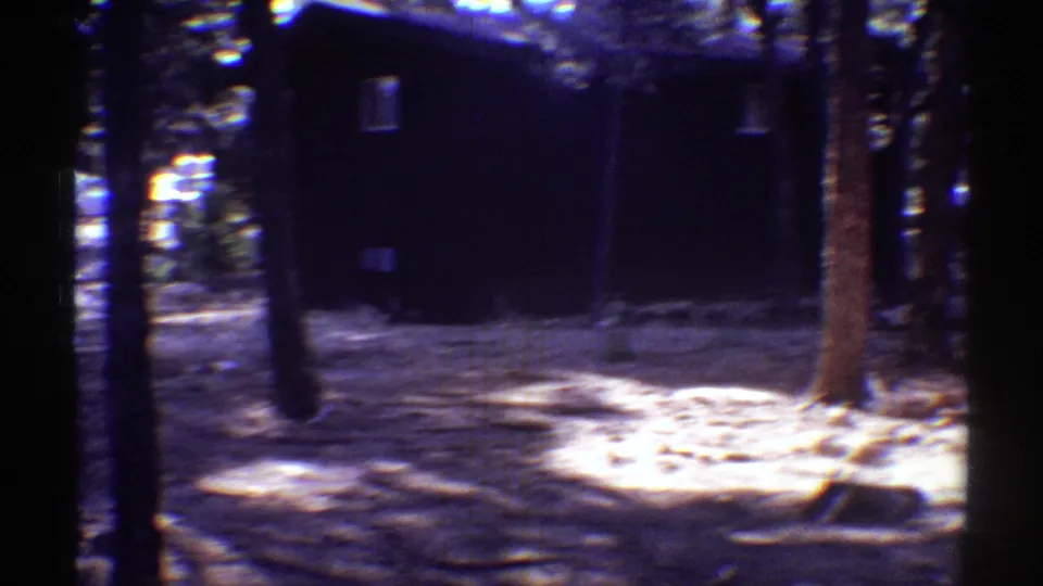 Handheld 8mm view of a shaded Arizona yard with trees, a dark wall or outbuilding, and bright patches of sunlight on the ground.