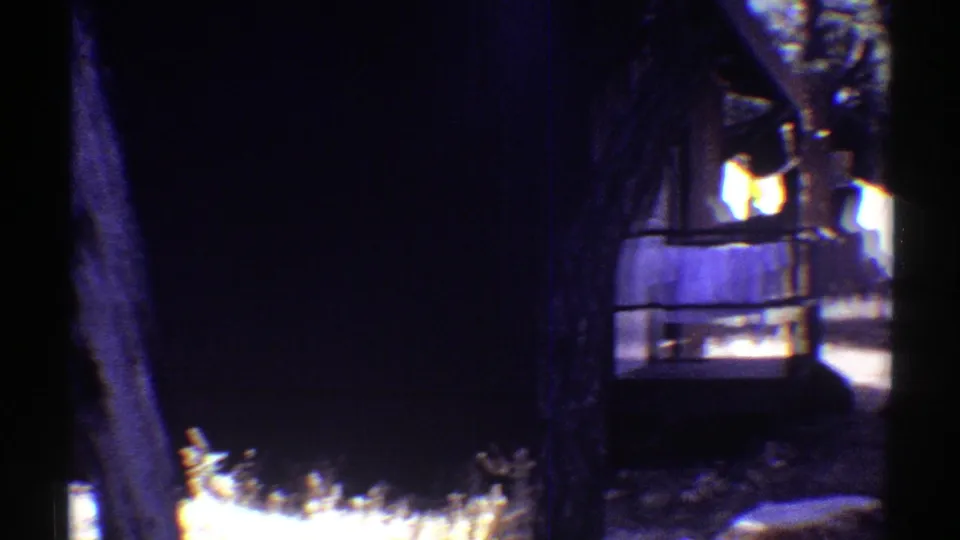 1969 Arizona 8mm frame showing a house exterior partly obscured by trees, with warm lit windows and heavy shadow.