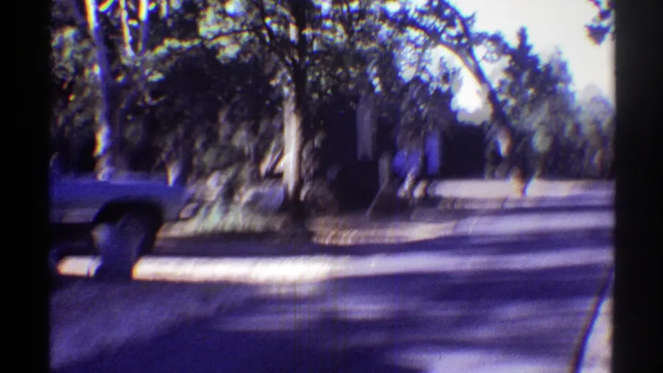 A resident appears near a parked vehicle on a quiet, tree-lined Arizona residential street in 1969 footage.