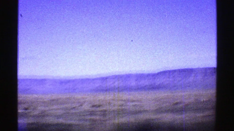Arizona 1969 home-movie frame showing dry open land and distant low hills under a pale blue sky.