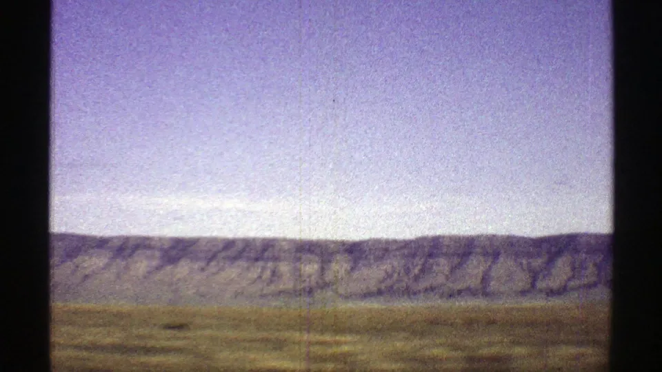 1969 Arizona 8mm travel view of a distant mountain ridge over open grassland, with visible film grain and border shadows.