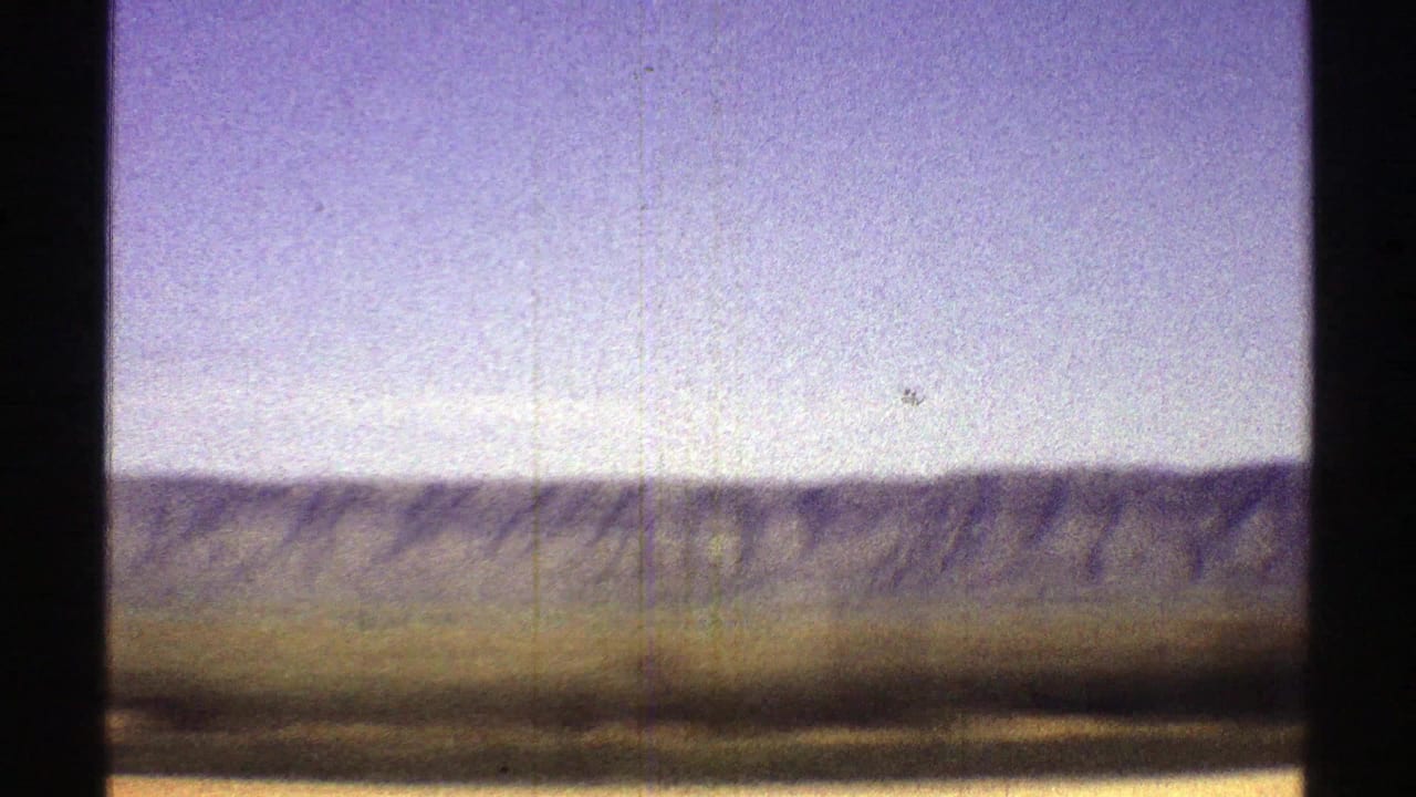 Pale sky above a distant desert ridge and flat foreground, bordered by dark film edges.