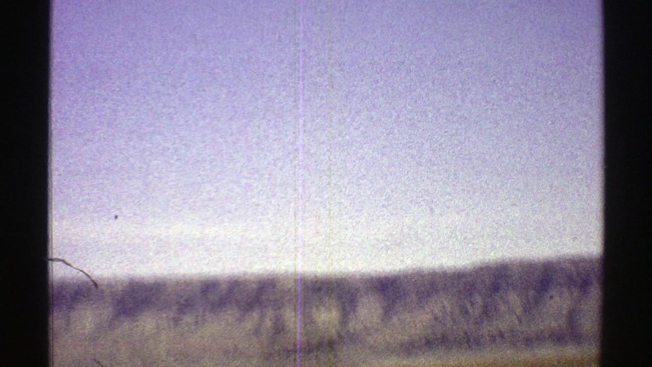 1969 Arizona desert view with a low mountain ridge, open sky, sparse foreground, and visible 8mm film scratches.