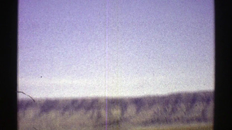 1969 Arizona desert view with a low mountain ridge, open sky, sparse foreground, and visible 8mm film scratches.