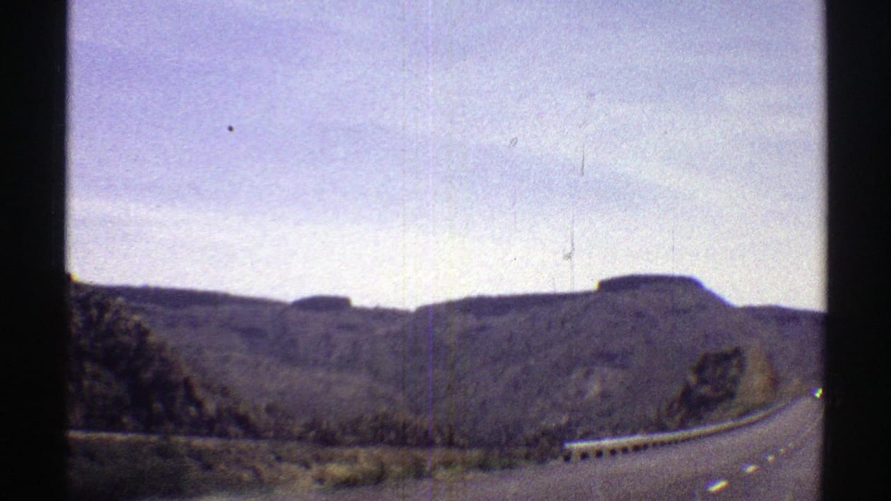 Road with guardrail running past layered desert hills.