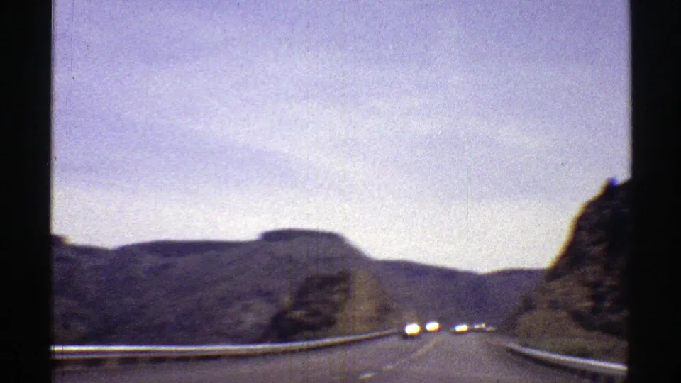 Arizona home-movie road view showing headlights on a curving highway between rocky roadside slopes.