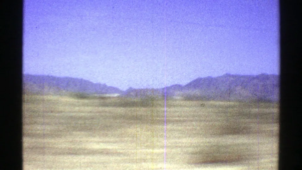 A wide 1969 Arizona desert view with flat open ground, distant blue-gray mountains, and a bright blue sky.