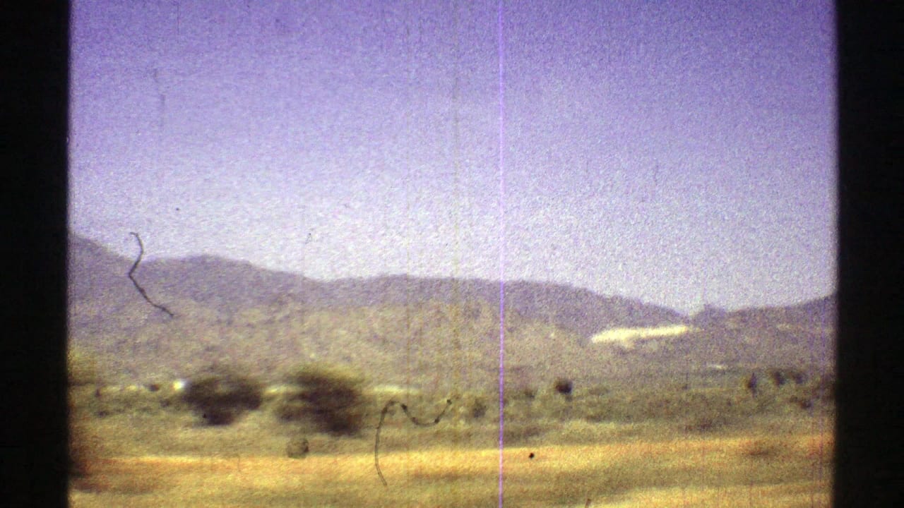 Mountain ridge and desert brush pass by behind dark film-frame borders.