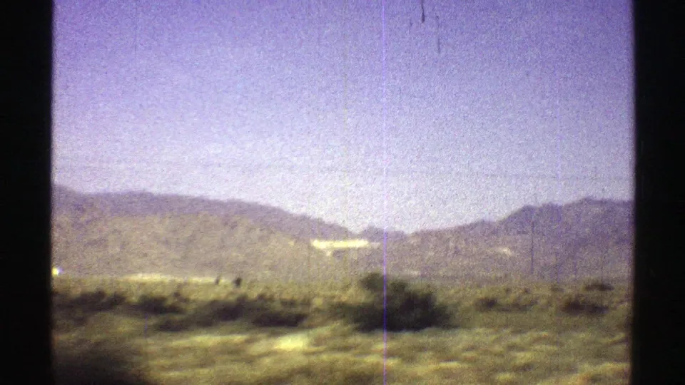 1969 Arizona home-movie frame of desert brush and mountain slopes from a moving car, with scratches and color shift visible.