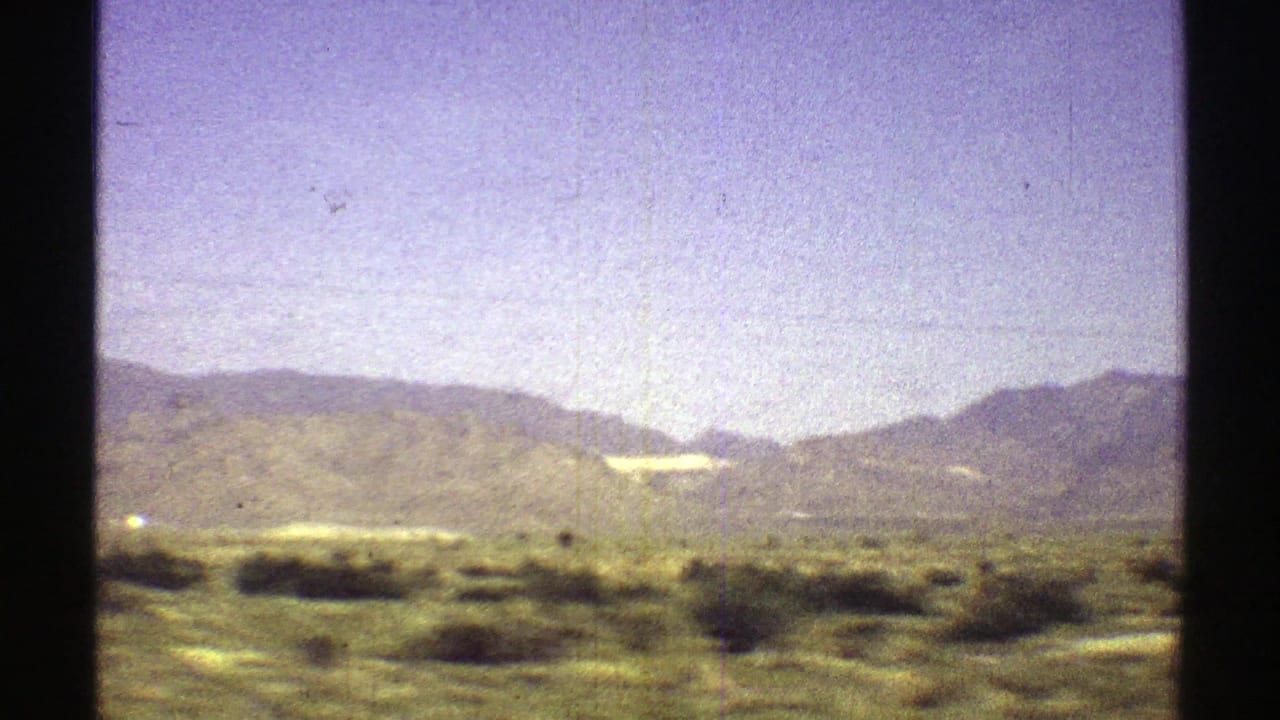 Desert scrub and low mountains under a hazy sky, seen through 8mm film gate edges.