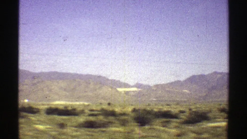 Arizona 1969 home-movie frame showing scrubland, green-brown hills, and distant mountains under a hazy blue-purple sky.