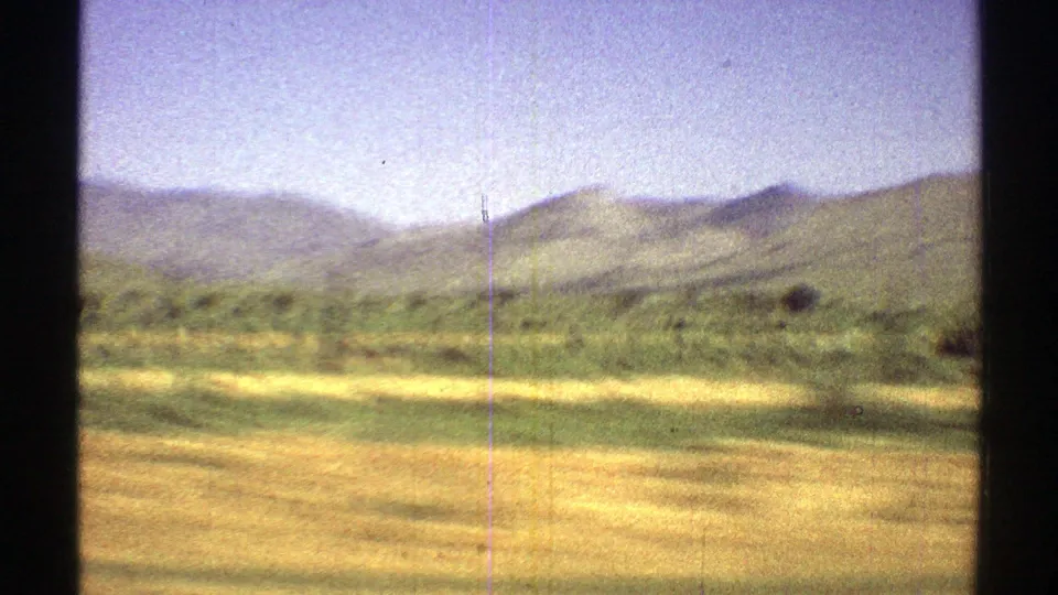 Arizona 1969 home-movie frame with dry foreground, scattered scrub, and rounded green hills in soft 8mm color.