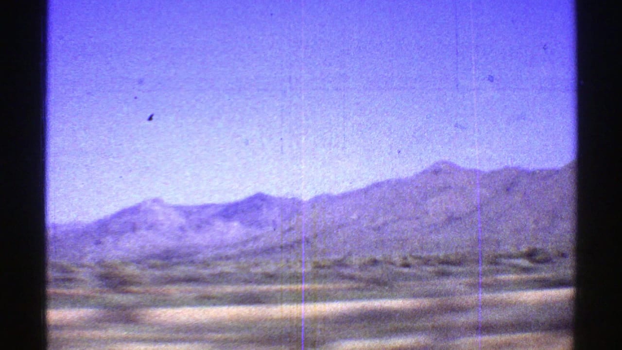 1969 Arizona 8mm frame looking across a low desert plain toward softened mountain ridges, with film scratches and color fading visible.