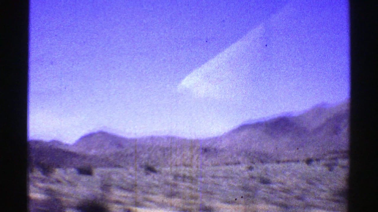 1969 Arizona 8mm frame showing a desert roadside, sparse brush, and low mountains viewed through dark vehicle-window framing.
