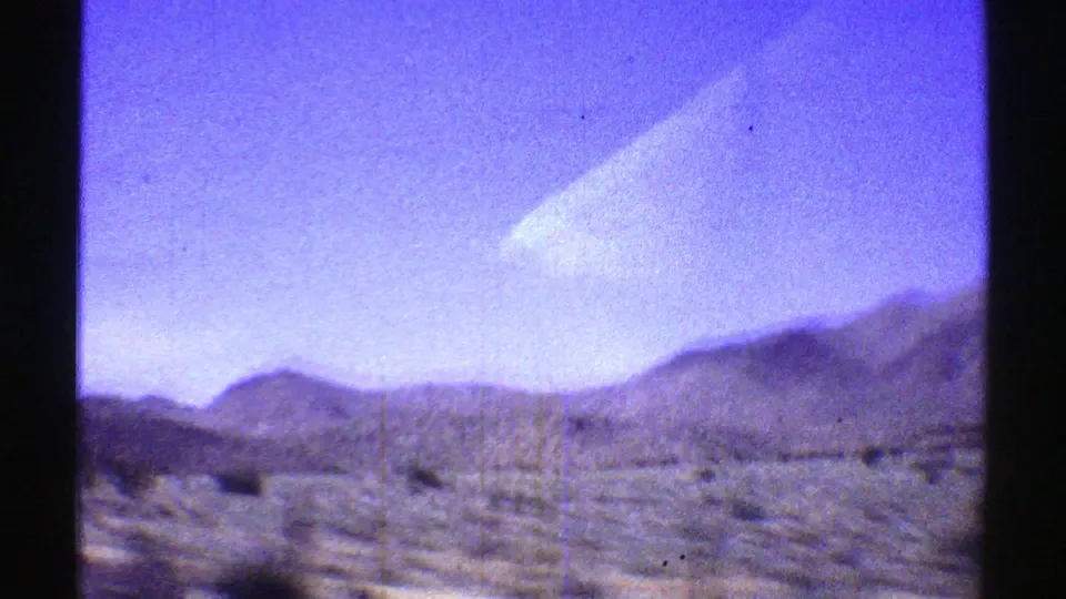 1969 Arizona 8mm frame showing a desert roadside, sparse brush, and low mountains viewed through dark vehicle-window framing.