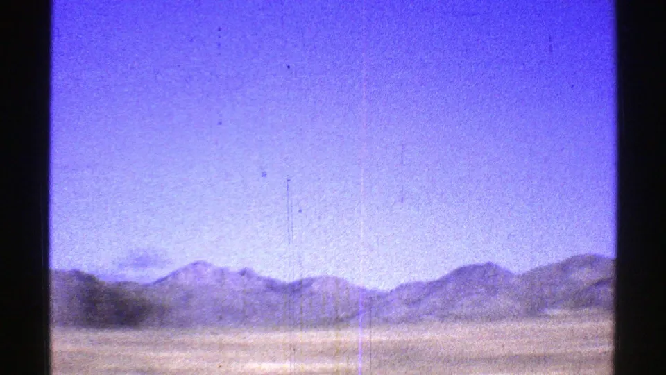 A broad Arizona desert view from the 1969 home movie shows sandy ground, low brush, and distant mountain ridges.
